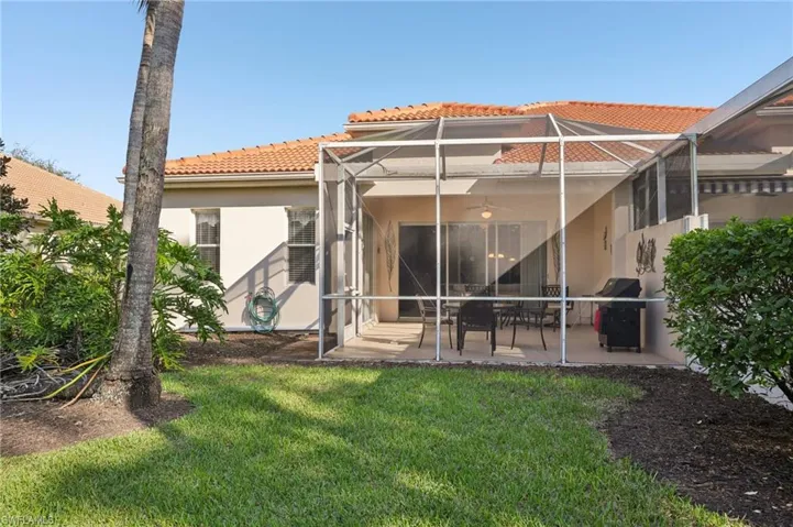 Rear view of property featuring glass enclosure, a ceiling fan, a patio area, a yard, and a tile roof