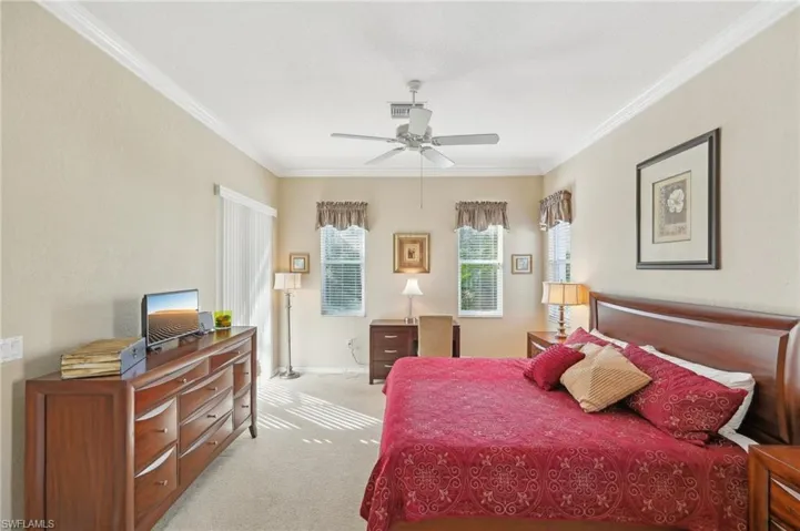 Bedroom with ornamental molding, visible vents, baseboards, ceiling fan, and light colored carpet