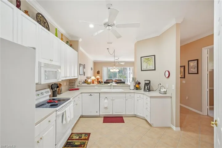 Kitchen with a sink, a peninsula, light countertops, and white appliances