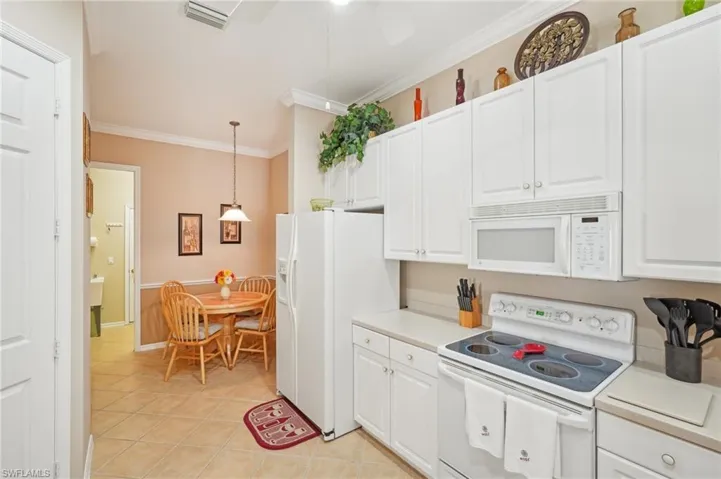 Kitchen with pendant lighting, light countertops, white cabinetry, and white appliances