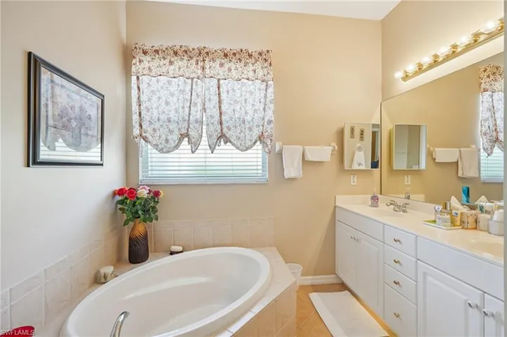 Bathroom with a sink, a garden tub, baseboards, double vanity, and tile patterned flooring