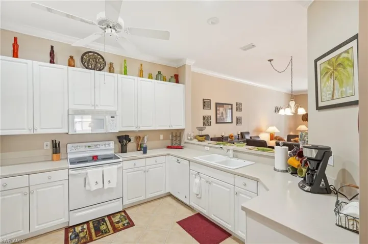 Kitchen with ornamental molding, a sink, white cabinetry, light countertops, and white appliances