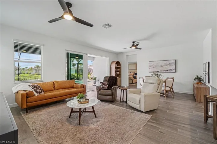 Spacious living area featuring wood-finish flooring, two modern ceiling fans with integrated lighting, and a window with horizontal blinds