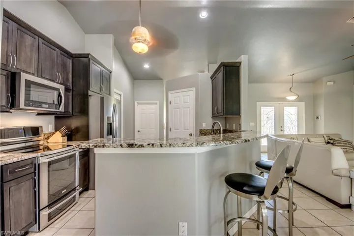 Kitchen with ceiling fan, dishwasher, lofted ceiling, light stone counters, and dark brown cabinets