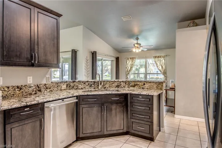 Kitchen featuring appliances with stainless steel finishes, light tile patterned floors, light stone countertops, dark brown cabinets, and recessed lighting