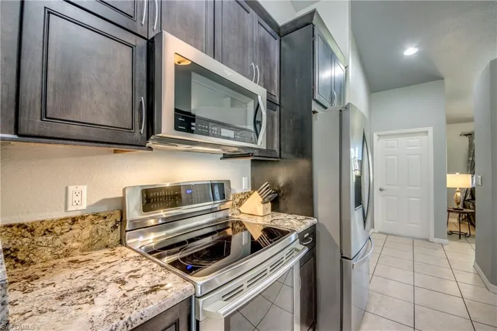 Kitchen featuring stainless steel appliances, light tile patterned flooring, dark brown cabinets, light stone counters, and a breakfast bar
