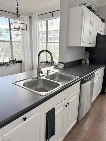 Kitchen featuring dishwasher, decorative light fixtures, white cabinetry, dark hardwood / wood-style flooring, and sink