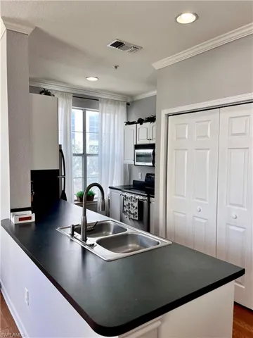 Kitchen with sink, white cabinetry, crown molding, appliances with stainless steel finishes, and kitchen peninsula