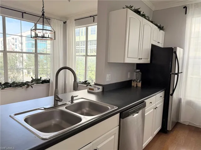 Kitchen with white cabinetry, stainless steel appliances, sink, hanging light fixtures, and crown molding