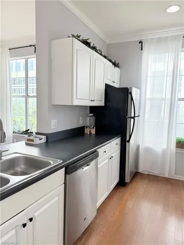 Kitchen with white cabinetry, stainless steel appliances, sink, ornamental molding, and light wood-type flooring