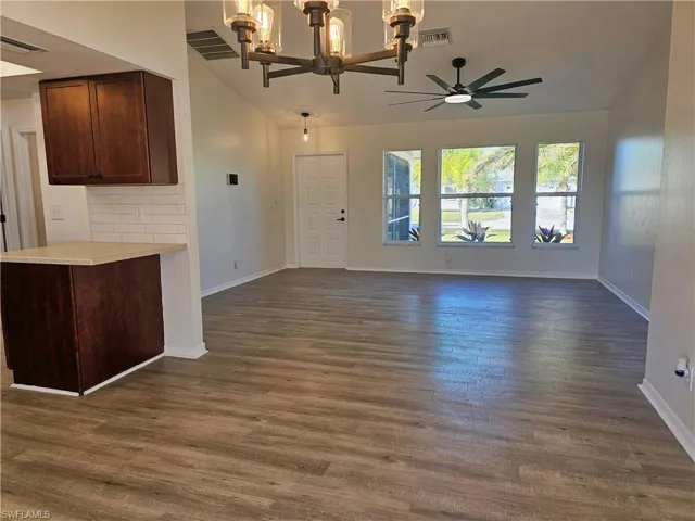 Unfurnished living room with a chandelier, dark wood-style floors, lofted ceiling, and ceiling fan