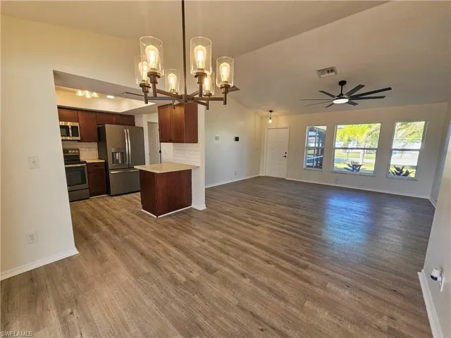 Kitchen with open floor plan, light countertops, hanging light fixtures, appliances with stainless steel finishes, and dark wood-style floors