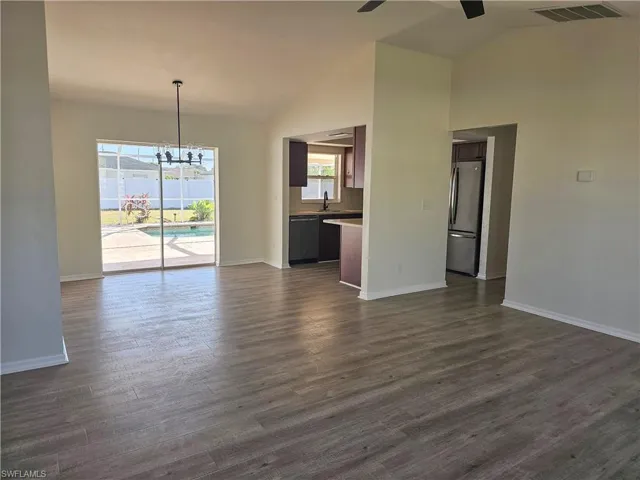 Unfurnished living room with a chandelier, dark wood-type flooring, a ceiling fan, and high vaulted ceiling