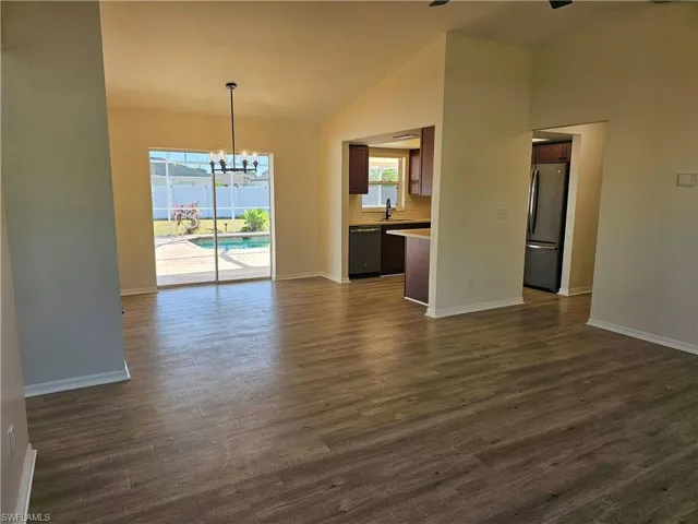Unfurnished dining area featuring a chandelier, dark wood-style flooring, and high vaulted ceiling