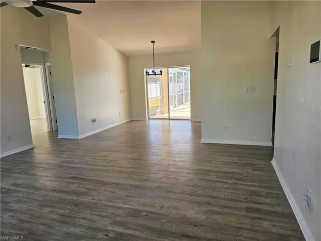 Empty room featuring dark wood-type flooring, a chandelier, a ceiling fan, and high vaulted ceiling
