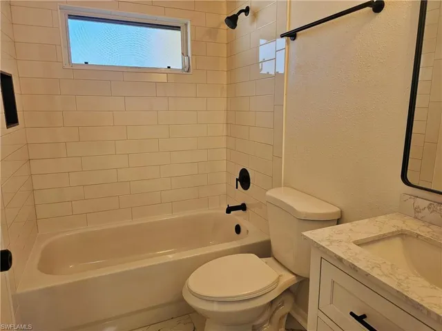 Bathroom with a textured wall, vanity, plenty of natural light, and shower / bath combination