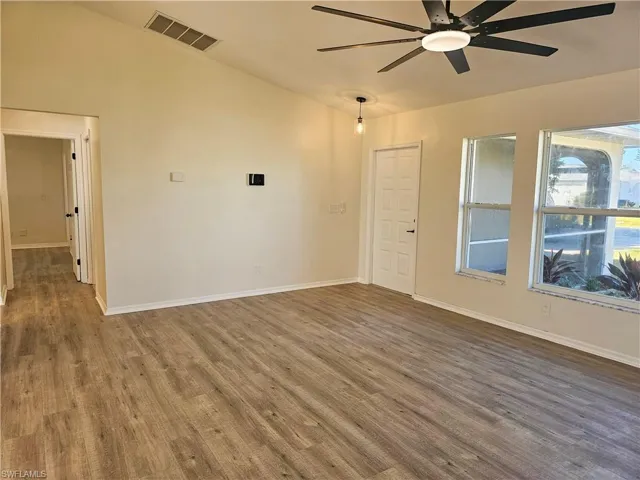 Spare room featuring vaulted ceiling, dark wood-style floors, and a ceiling fan