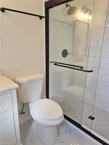 Full bathroom with marble finish floors, vanity, a shower stall, and a textured wall