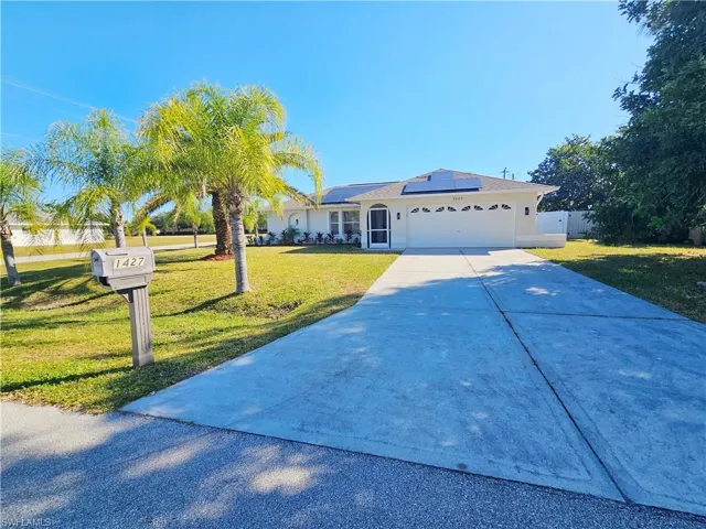 Single story home featuring solar panels, concrete driveway, a front yard, a garage, and stucco siding