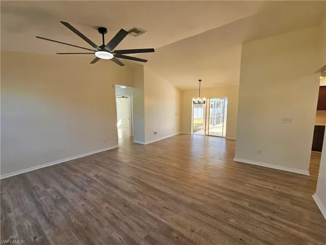 Empty room with a chandelier, vaulted ceiling, dark wood-style flooring, and a ceiling fan