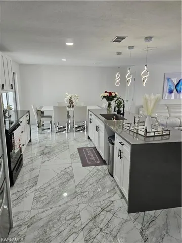 Kitchen with white cabinets, decorative light fixtures, a kitchen island with sink, and sink