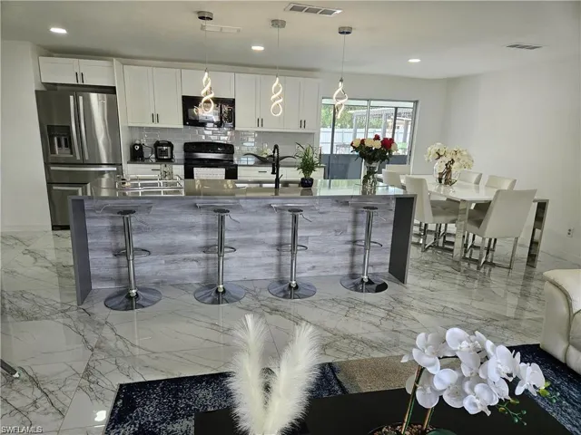 Bar with backsplash, sink, black appliances, white cabinetry, and hanging light fixtures