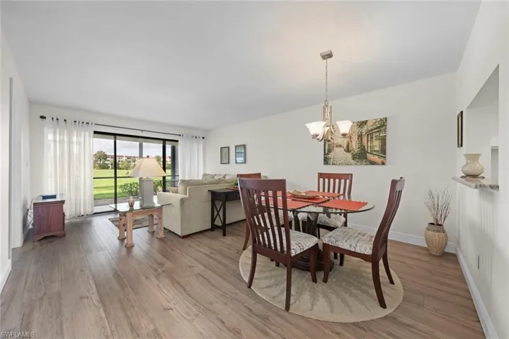 Open-concept living and dining area featuring vinyl flooring, a chandelier, and a pass-through window with a stone counter sill