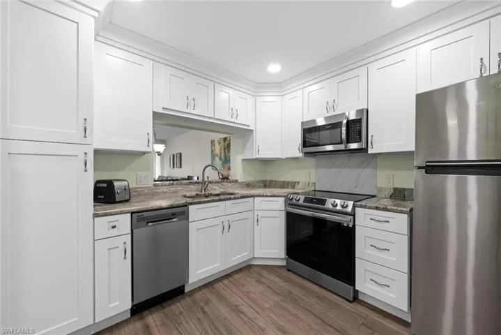 Modern kitchen featuring white shaker-style cabinetry, stainless steel appliances, granite countertops, and vinyl flooring