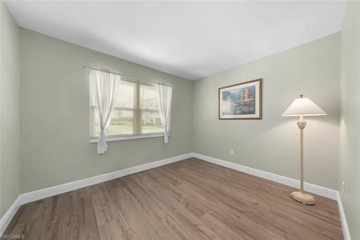 Bedroom featuring luxury vinyl flooring, a window with blinds and sheer curtains, light green painted walls, and white baseboards