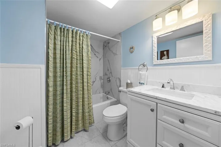Bathroom featuring a white vanity with a stone countertop, an undermount sink, a combination tub and shower, and a white framed mirror