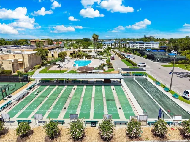 Expansive outdoor recreational area featuring multiple shuffleboard courts, a covered seating area, a large swimming pool, and tennis courts