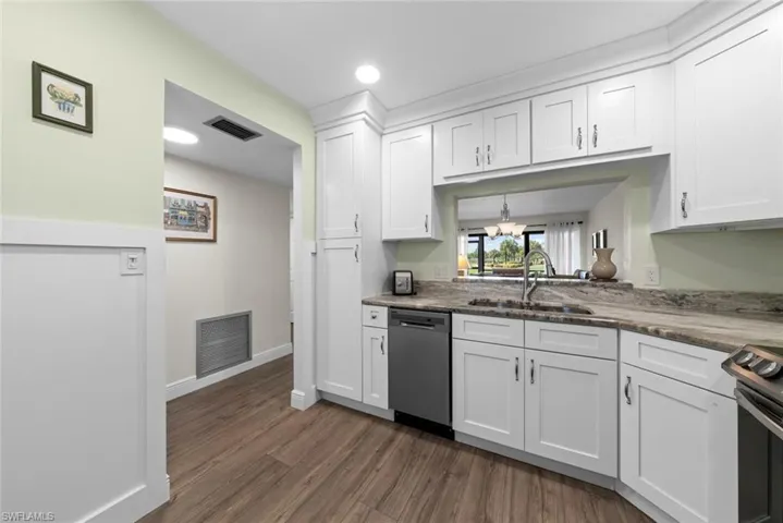 Kitchen featuring white shaker-style cabinetry, a stainless steel dishwasher, a stainless steel gooseneck faucet, a stone countertop, and luxury vinyl flooring