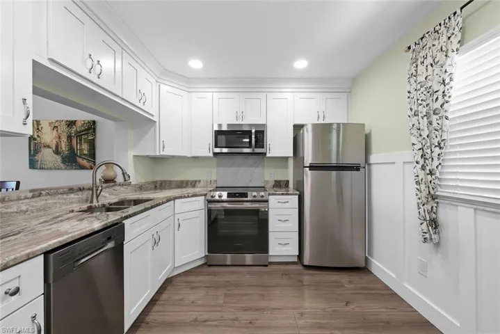 Kitchen featuring white shaker cabinetry, stainless steel appliances, a double basin sink with an arched faucet, and vinyl flooring