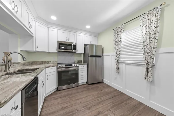 Kitchen featuring white cabinetry, stone countertops, stainless steel appliances, vinyl flooring, and wainscoting