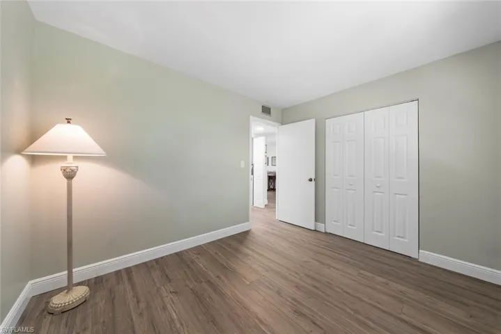 Bedroom featuring luxury vinyl flooring, white trim, a white door, and white bi-fold closet doors