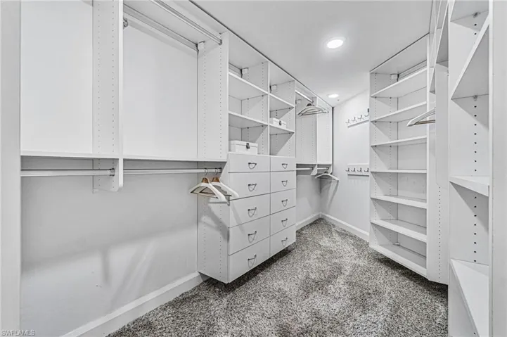Spacious walk in primary closet featuring abundant custom built-in storage and shelving areas.