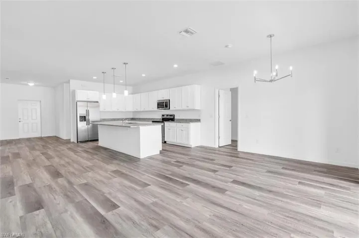 Kitchen featuring appliances with stainless steel finishes, open floor plan, a chandelier, light wood-type flooring, and recessed lighting