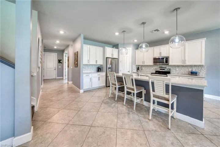 Kitchen with white cabinets, decorative light fixtures, stainless steel appliances, a center island with sink, and tasteful backsplash