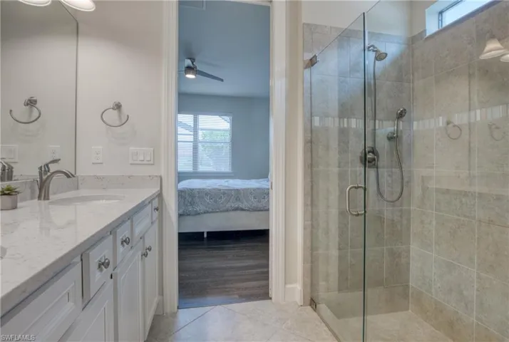 Bathroom with tile patterned flooring, ceiling fan, a shower with door, and vanity
