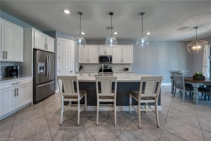 Kitchen with appliances with stainless steel finishes, white cabinetry, a notable chandelier, and decorative backsplash