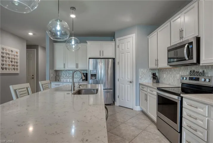 Kitchen featuring light stone countertops, appliances with stainless steel finishes, white cabinetry, and decorative light fixtures