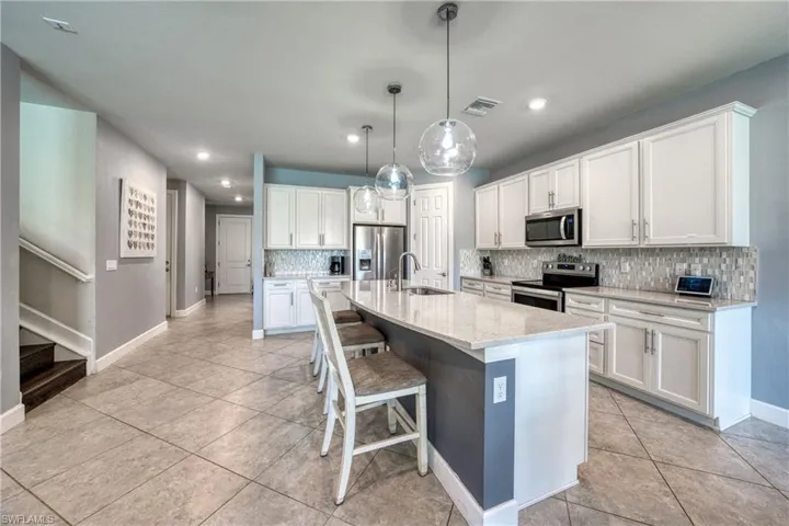 Kitchen with pendant lighting, an island with sink, decorative backsplash, appliances with stainless steel finishes, and white cabinets