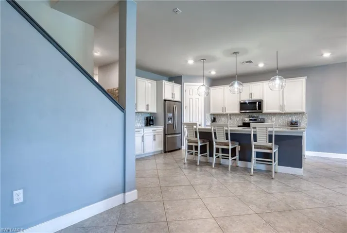 Kitchen with pendant lighting, stainless steel appliances, white cabinetry, and a kitchen island with sink
