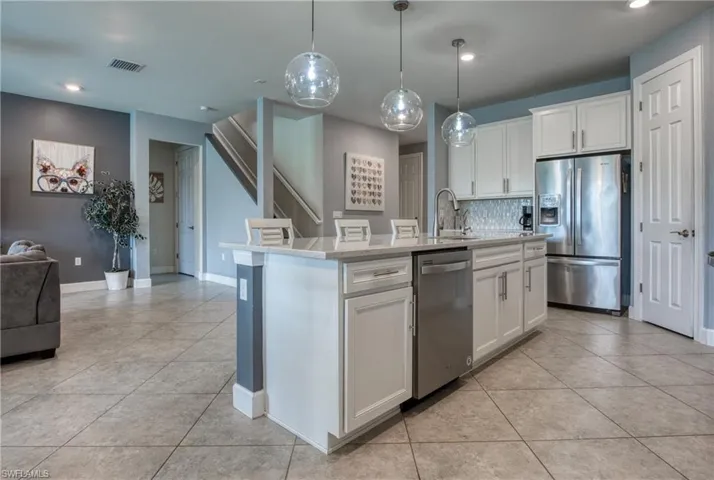 Kitchen featuring tasteful backsplash, appliances with stainless steel finishes, white cabinetry, and a kitchen island with sink