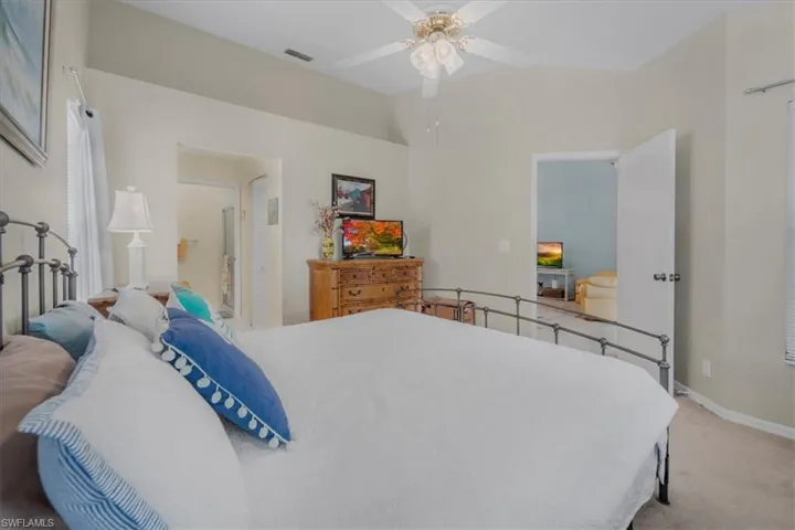 Bedroom with light colored carpet, vaulted ceiling, ceiling fan, and ensuite bathroom