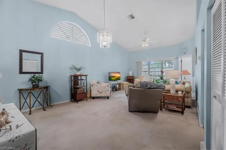 Living room with lofted ceiling, light colored carpet, a ceiling fan, and a chandelier