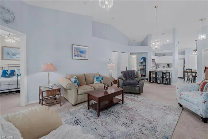 Living room with light colored carpet, a ceiling fan, lofted ceiling, and hanging lights