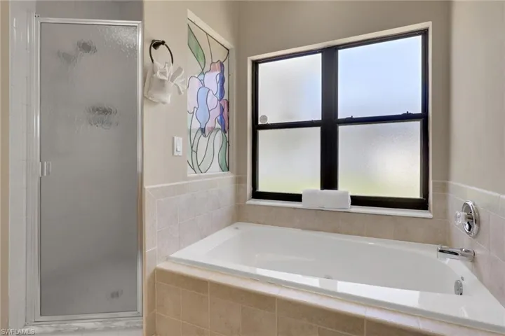 Soaking tub with tiled surround, adjacent to a frosted window and a stained glass accent panel