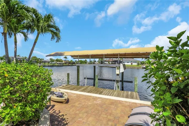 Waterfront patio with brick paver flooring, leading to a wooden dock with a boat lift and canopy