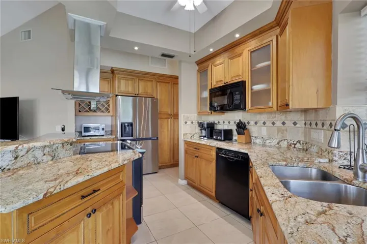 Kitchen featuring light wood cabinetry, stone countertops, a stainless steel double sink, and a tiled backsplash